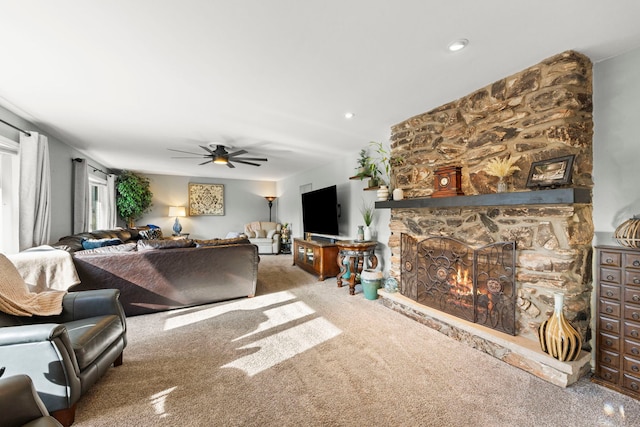 carpeted living room with a stone fireplace and ceiling fan