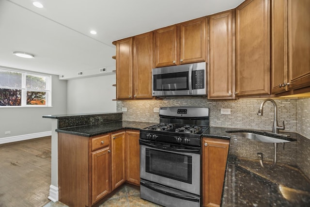 kitchen featuring sink, stainless steel appliances, kitchen peninsula, dark stone countertops, and light hardwood / wood-style floors