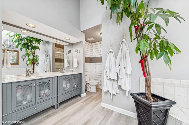 full bath with double vanity, wood finished floors, a sink, and toilet