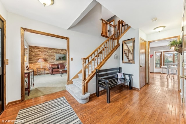 stairs with baseboards, brick wall, and wood finished floors