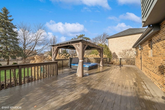 deck with an outdoor hot tub, fence, and a gazebo