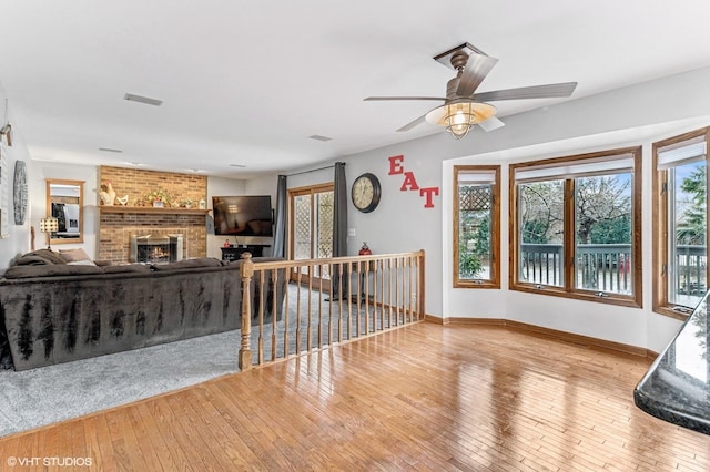 living area featuring visible vents, baseboards, light wood-style floors, ceiling fan, and a brick fireplace