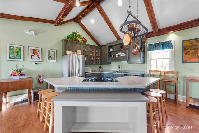 kitchen with stainless steel fridge, light wood-type flooring, vaulted ceiling with beams, black electric cooktop, and a center island