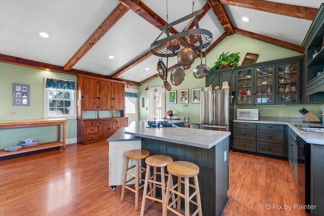 kitchen with lofted ceiling with beams, a center island, appliances with stainless steel finishes, and light hardwood / wood-style flooring