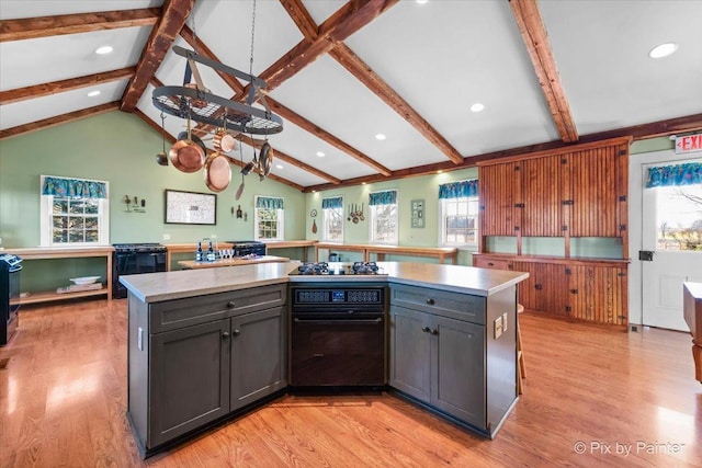 kitchen with light wood-type flooring, lofted ceiling with beams, a kitchen island, and a wealth of natural light