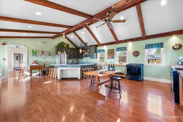 kitchen featuring ceiling fan, lofted ceiling with beams, stainless steel fridge, hardwood / wood-style floors, and a breakfast bar