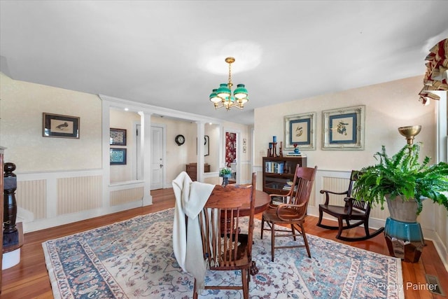 dining room with hardwood / wood-style floors, decorative columns, and an inviting chandelier