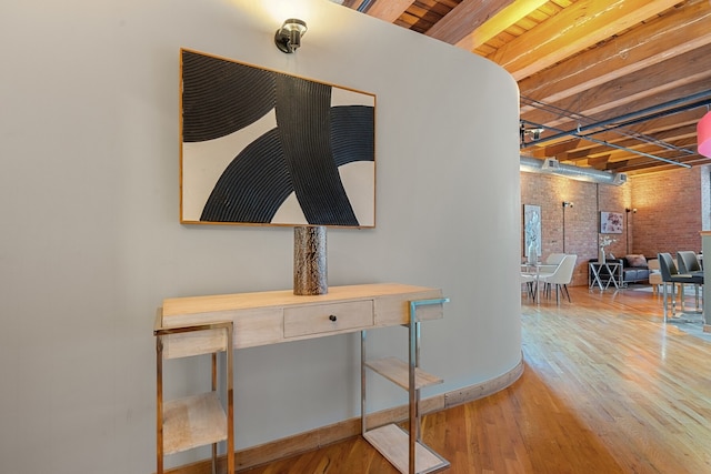 hall with beamed ceiling, light hardwood / wood-style floors, wood ceiling, and brick wall