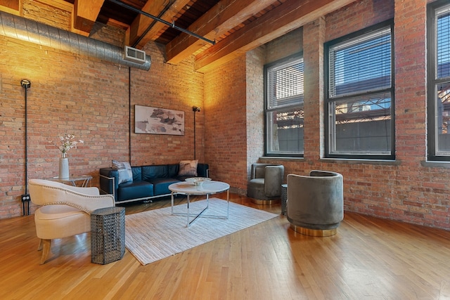 living room featuring hardwood / wood-style flooring, beam ceiling, a towering ceiling, and brick wall