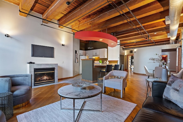 living room with beamed ceiling, wooden ceiling, light wood-type flooring, and a tiled fireplace