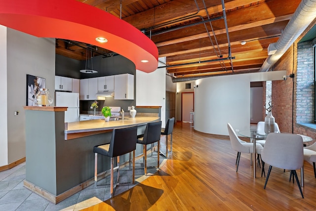 kitchen featuring white cabinetry, beamed ceiling, brick wall, white appliances, and light wood-type flooring