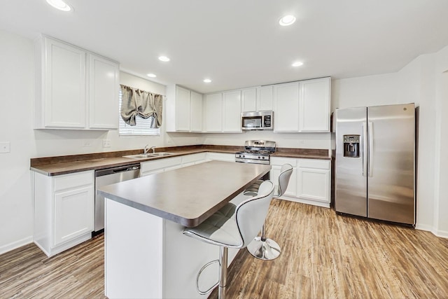 kitchen featuring light wood-type flooring, stainless steel appliances, sink, white cabinets, and a center island