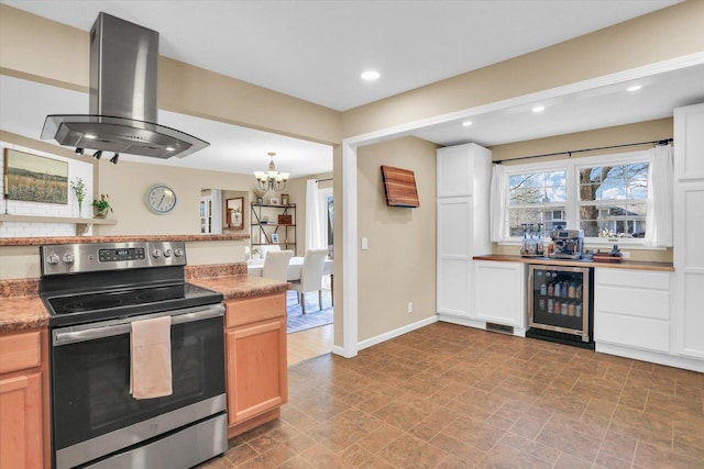 kitchen featuring island exhaust hood, stainless steel electric range oven, a notable chandelier, white cabinets, and wine cooler