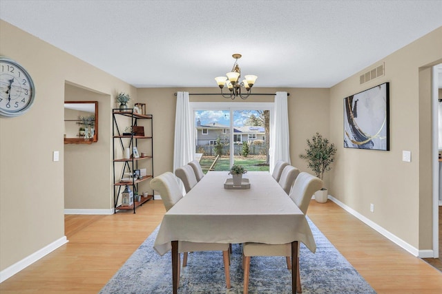 dining area with a textured ceiling, light hardwood / wood-style flooring, and an inviting chandelier