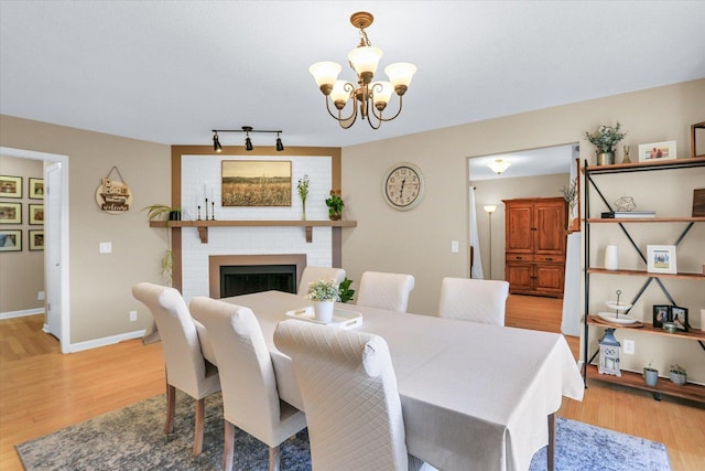 dining space with an inviting chandelier, a brick fireplace, and light hardwood / wood-style flooring