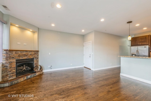 unfurnished living room with a stone fireplace and dark wood-type flooring