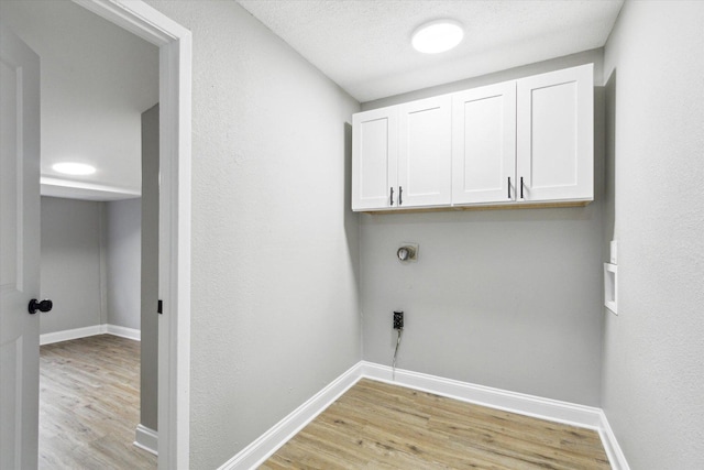 laundry room featuring electric dryer hookup, light hardwood / wood-style flooring, cabinets, and a textured ceiling