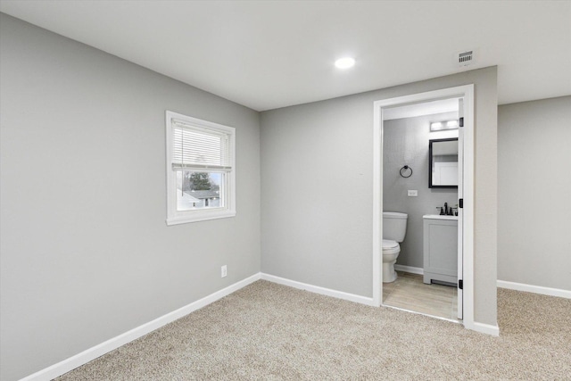 unfurnished bedroom featuring connected bathroom, light carpet, and sink