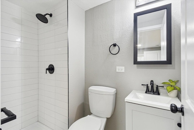 bathroom with a tile shower, vanity, and toilet