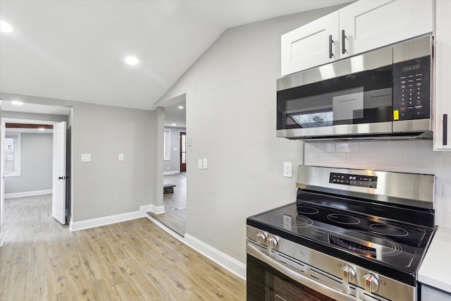 kitchen featuring backsplash, stainless steel appliances, vaulted ceiling, white cabinets, and light hardwood / wood-style floors