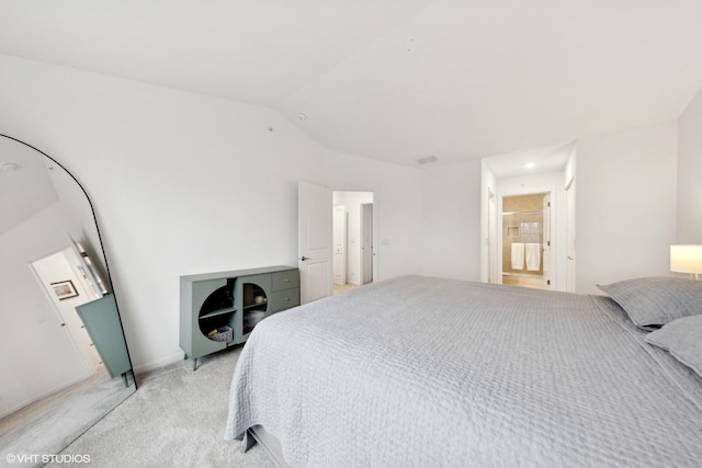 bedroom with ensuite bathroom, light colored carpet, and vaulted ceiling