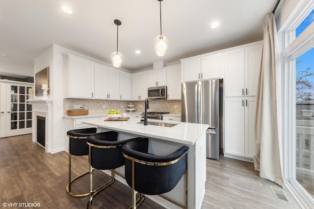 kitchen featuring a kitchen island with sink, sink, decorative light fixtures, white cabinetry, and stainless steel appliances