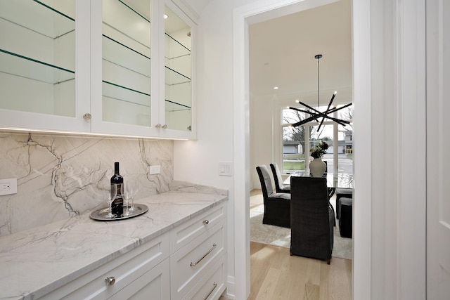 bar featuring light stone countertops, light wood-type flooring, backsplash, pendant lighting, and white cabinetry