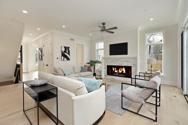 living room with ceiling fan, crown molding, a fireplace, and light hardwood / wood-style flooring