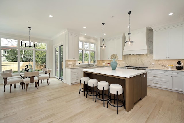 kitchen with white cabinetry, a center island, hanging light fixtures, light hardwood / wood-style floors, and custom range hood