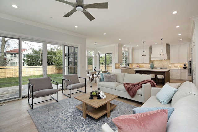 living room featuring ceiling fan with notable chandelier, a healthy amount of sunlight, light wood-type flooring, and crown molding