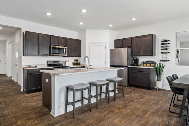 kitchen featuring sink, dark hardwood / wood-style floors, an island with sink, a kitchen bar, and appliances with stainless steel finishes