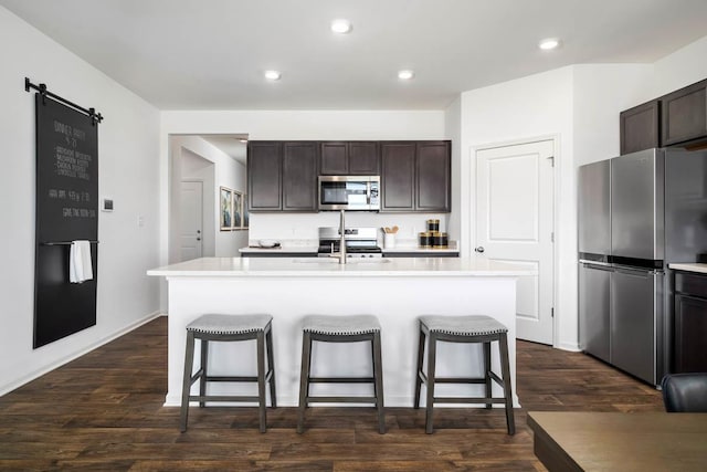 kitchen with dark wood-type flooring, stainless steel appliances, and an island with sink