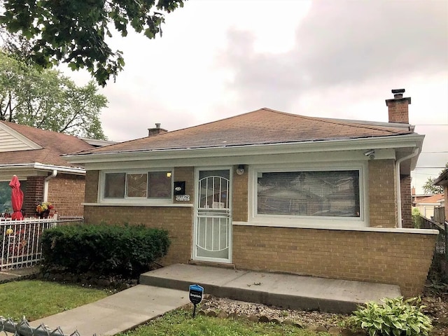 view of front facade with brick siding, a chimney, and fence