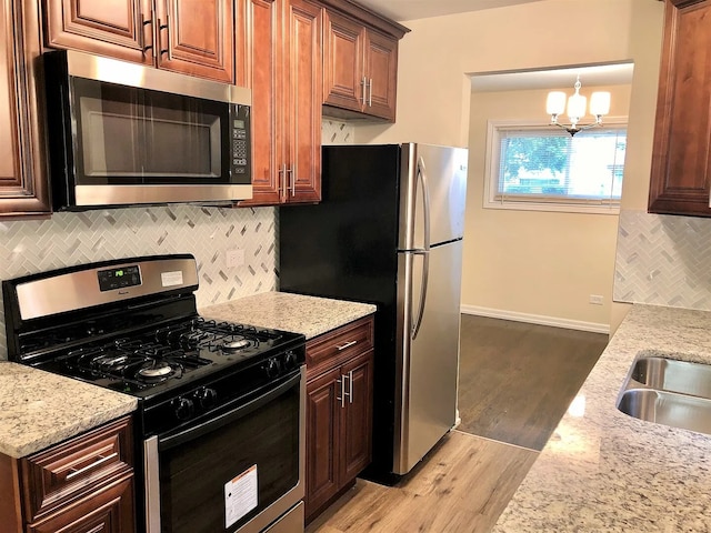 kitchen with light stone counters, light wood finished floors, stainless steel appliances, tasteful backsplash, and an inviting chandelier