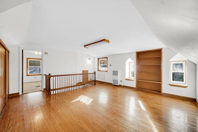 additional living space with heating unit, light hardwood / wood-style flooring, and lofted ceiling