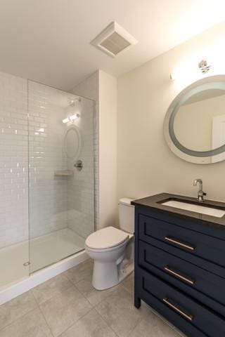 bathroom with tiled shower, tile patterned flooring, vanity, and toilet