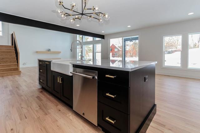 kitchen featuring a kitchen island with sink, sink, decorative light fixtures, dishwasher, and light hardwood / wood-style floors