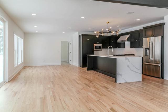 kitchen with backsplash, stainless steel appliances, light hardwood / wood-style flooring, a chandelier, and an island with sink