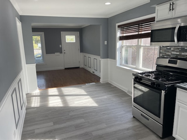 kitchen featuring decorative backsplash, appliances with stainless steel finishes, crown molding, light hardwood / wood-style floors, and white cabinetry