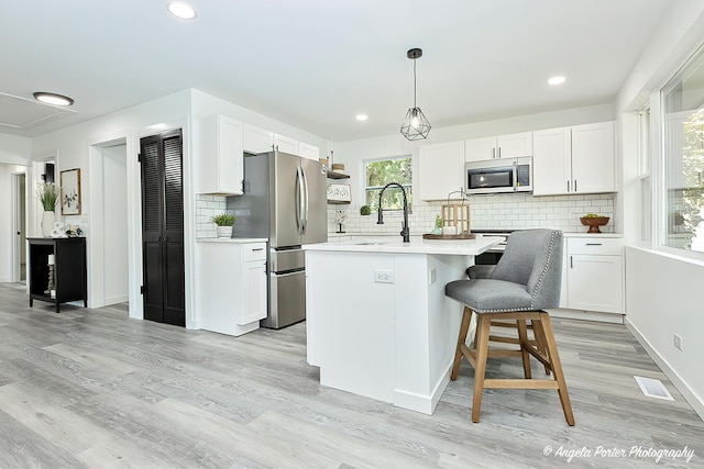 kitchen featuring a kitchen island with sink, white cabinets, stainless steel appliances, and light wood-type flooring