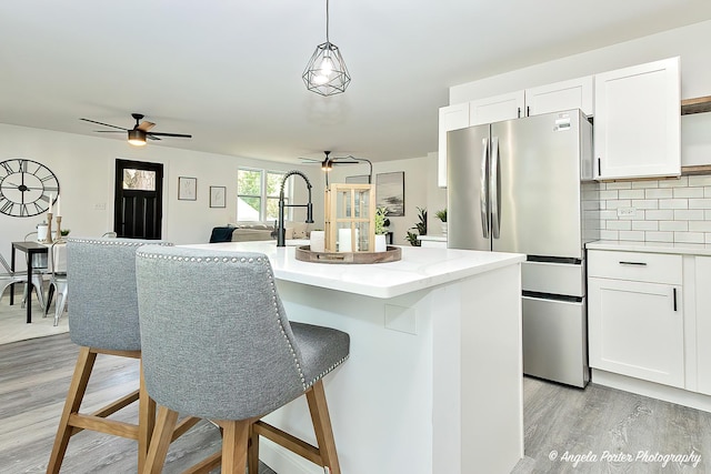 kitchen featuring white cabinetry, hanging light fixtures, light hardwood / wood-style flooring, stainless steel fridge, and a kitchen island