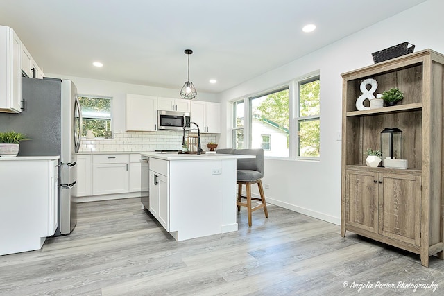 kitchen with appliances with stainless steel finishes, a wealth of natural light, pendant lighting, white cabinets, and an island with sink