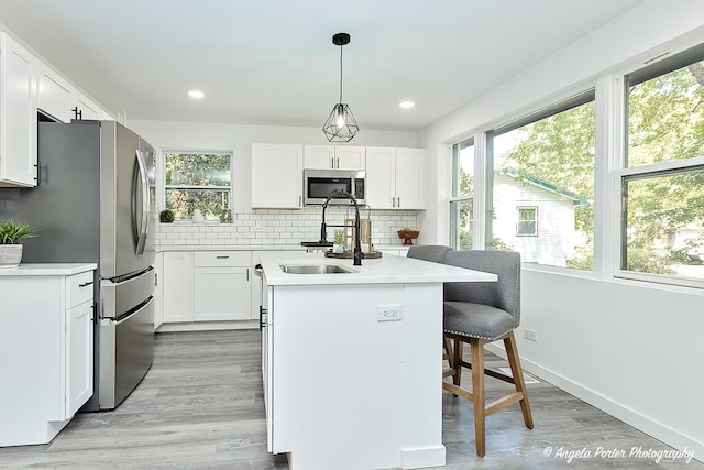 kitchen featuring a center island with sink, white cabinetry, stainless steel appliances, and plenty of natural light