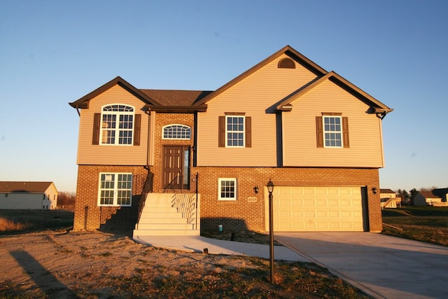 raised ranch featuring an attached garage, concrete driveway, and brick siding