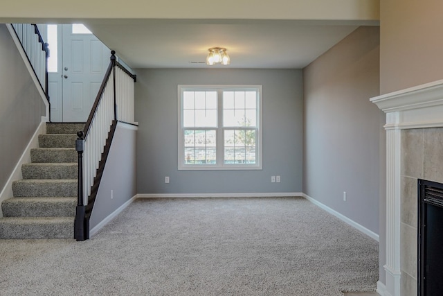 unfurnished living room featuring carpet floors, stairway, a tile fireplace, and baseboards