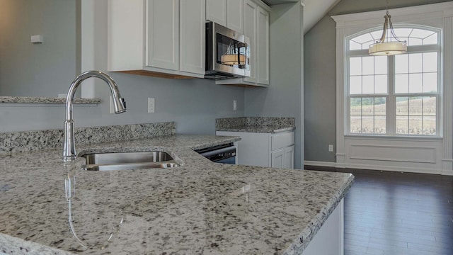 kitchen with light stone counters, pendant lighting, stainless steel microwave, white cabinetry, and a sink