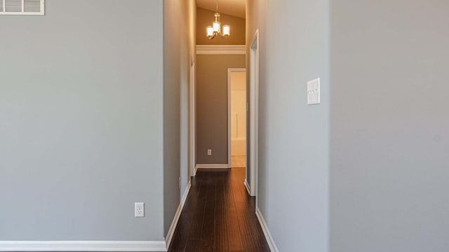 hallway with dark wood-style flooring, visible vents, a notable chandelier, and baseboards