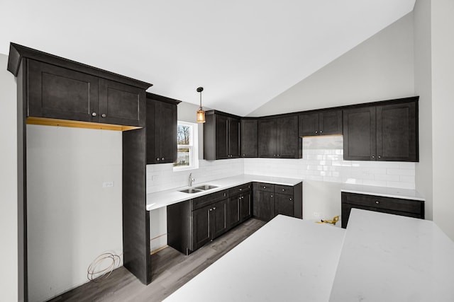 kitchen featuring hanging light fixtures, sink, light hardwood / wood-style flooring, backsplash, and lofted ceiling