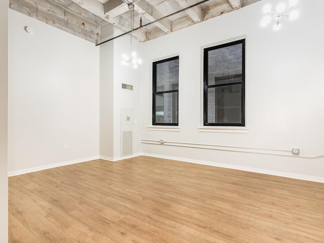 spare room featuring light wood-type flooring, a high ceiling, and a chandelier