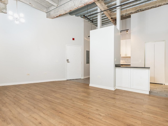 unfurnished living room with electric panel, light hardwood / wood-style flooring, a chandelier, and a high ceiling